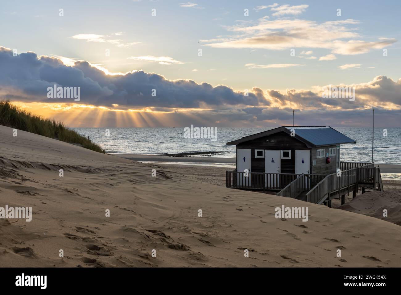 La costa di orth Sea al suo meglio: Raggi del sole, dune, molo e mare. Il sole che tramonta scompare dietro uno spesso strato di nuvole sospese. Foto Stock