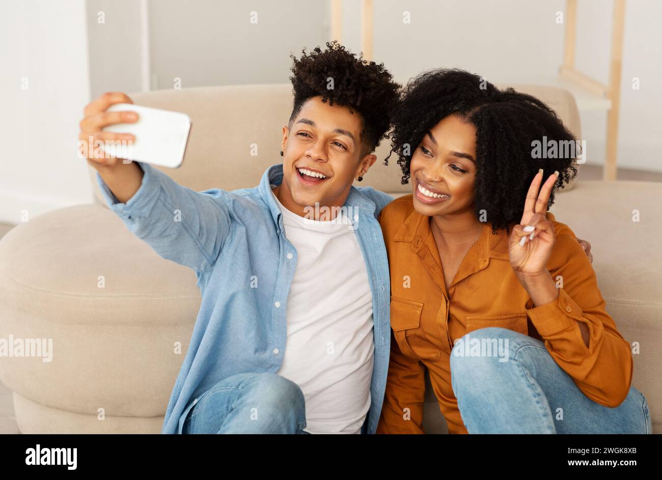Una giovane coppia allegra cattura un momento di gioia con un selfie, l'uomo con una camicia in denim che fa brillare un sorriso Foto Stock
