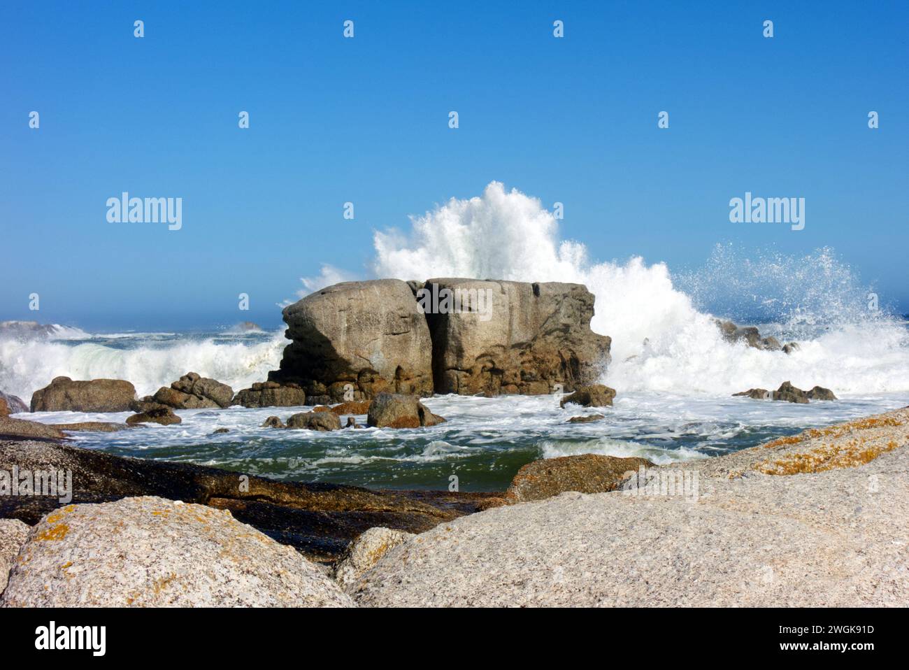 Onde che si infrangono contro le rocce sotto il cielo blu a Camps Bay, città del Capo, Sudafrica, Africa Foto Stock