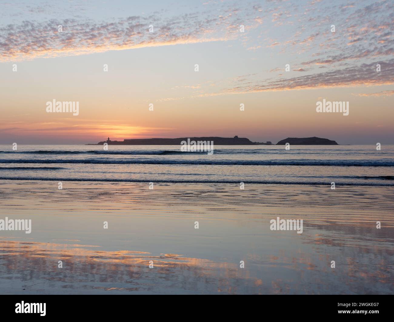 Tramonto su una spiaggia di sabbia con un'isola all'orizzonte mentre il cielo spettacolare si riflette nell'acqua di Essaouira, Marocco, 5 febbraio 2024 Foto Stock