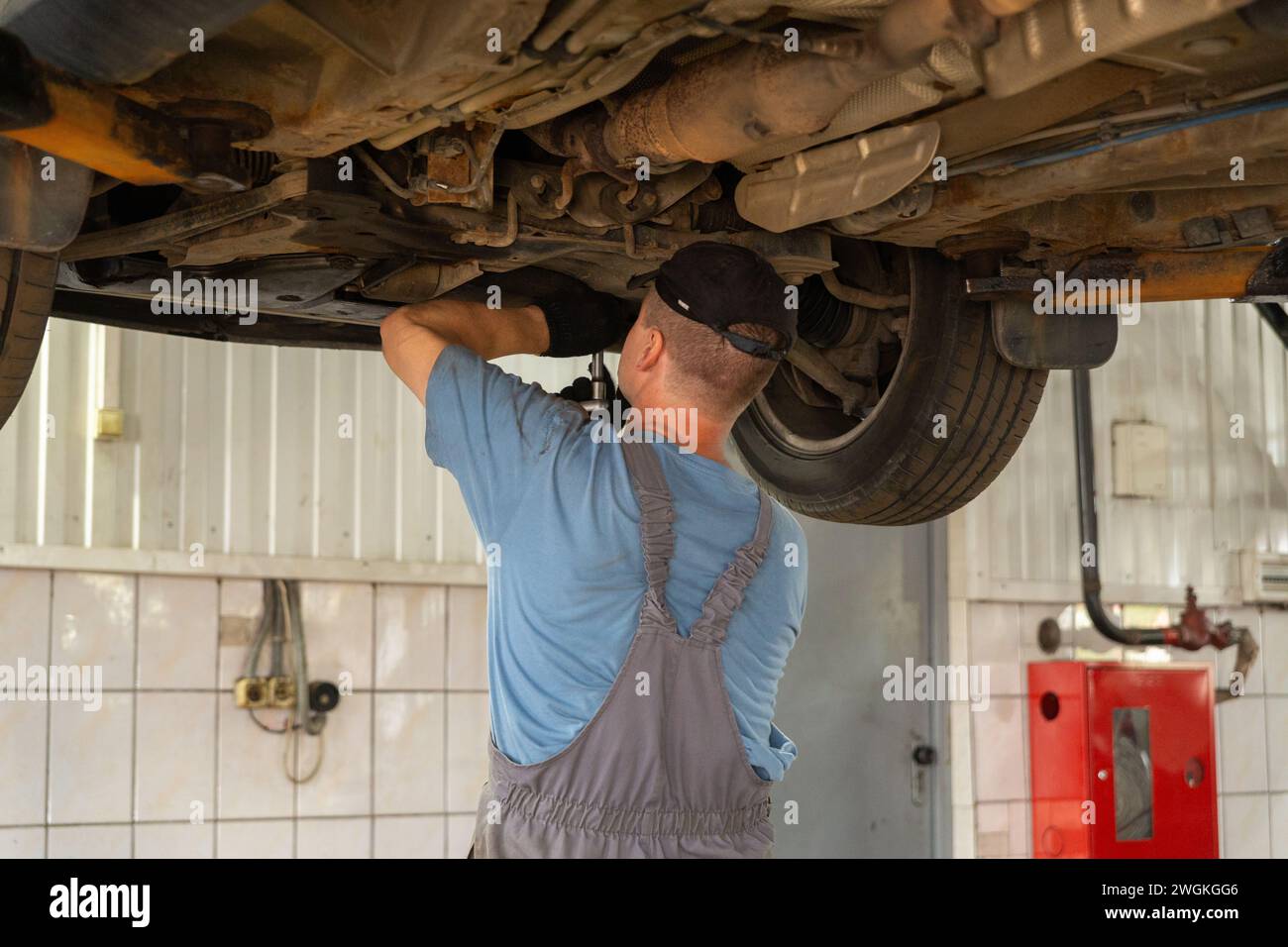 Meccanico di auto che lavora in officina di riparazione auto. Uomo in uniforme che lavora con il motore dell'auto. Foto Stock