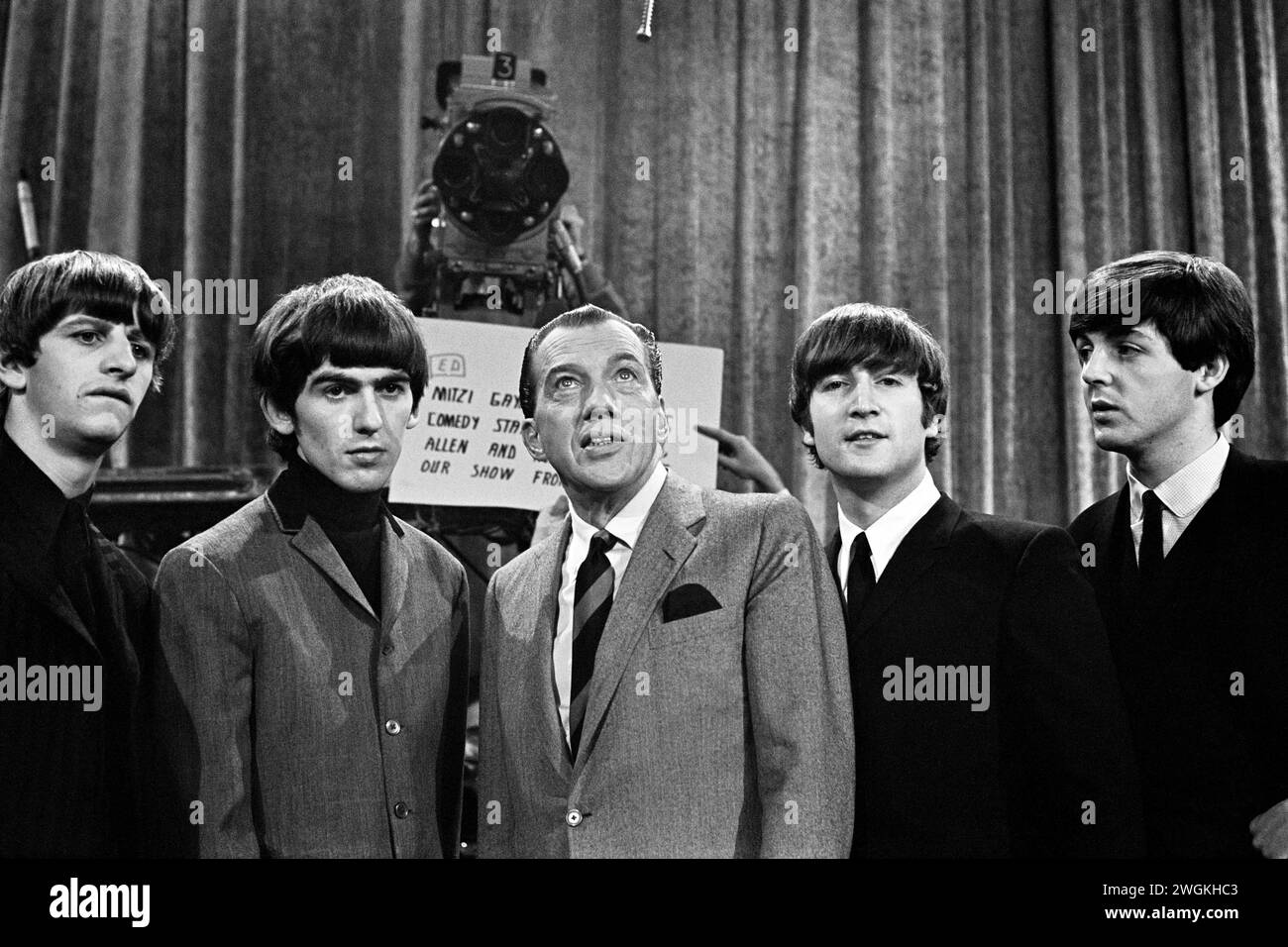 I Beatles e ed Sullivan posano di fronte a una telecamera della CBS e a un cartello con gli ospiti di Sullivan per lo spettacolo della settimana successiva da trasmettere dal Deauville Hotel di Miami Beach. Chiamata fotografica post-prove pomeridiana, sabato 8 febbraio 1964 CBS' The ed Sullivan Show CBS Studio 50, Broadway and West 53rd Street, New York, NY. Da L a R: Ringo Starr, George Harrison, ed Sullivan, John Lennon, Paul McCartney Foto Stock