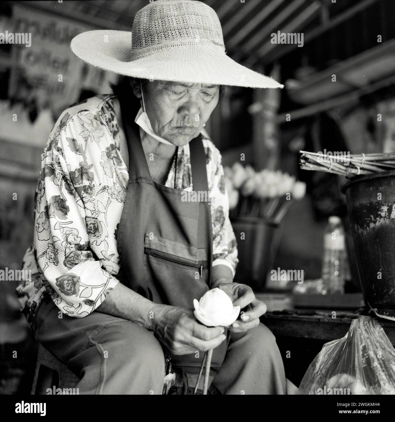 Vecchia signora che prepara fiori in vendita in un tempio buddista in Thailandia Foto Stock