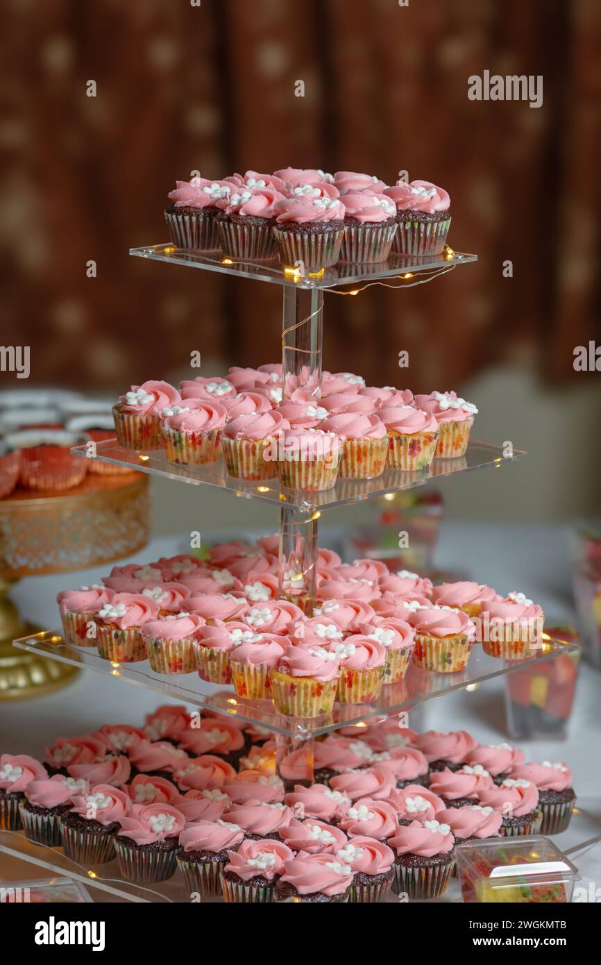 Cupcake di compleanno su un espositore in vetro a tre piani con fiore bianco rosa festoso Foto Stock