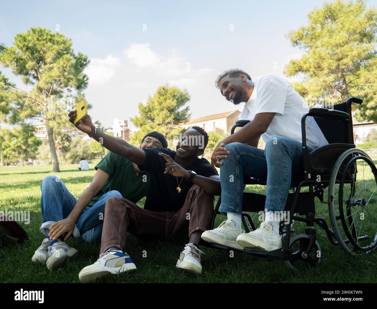 Gruppo di giovani amici maschi diversi uno di loro su una sedia a rotelle che si fa un selfie in un parco Foto Stock