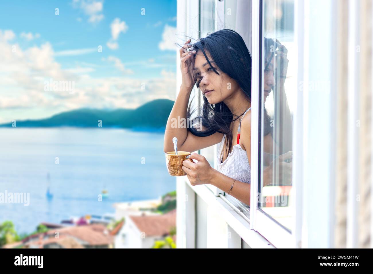 Una donna in abito estivo tiene una tazza in una finestra aperta di un edificio in una destinazione turistica Foto Stock