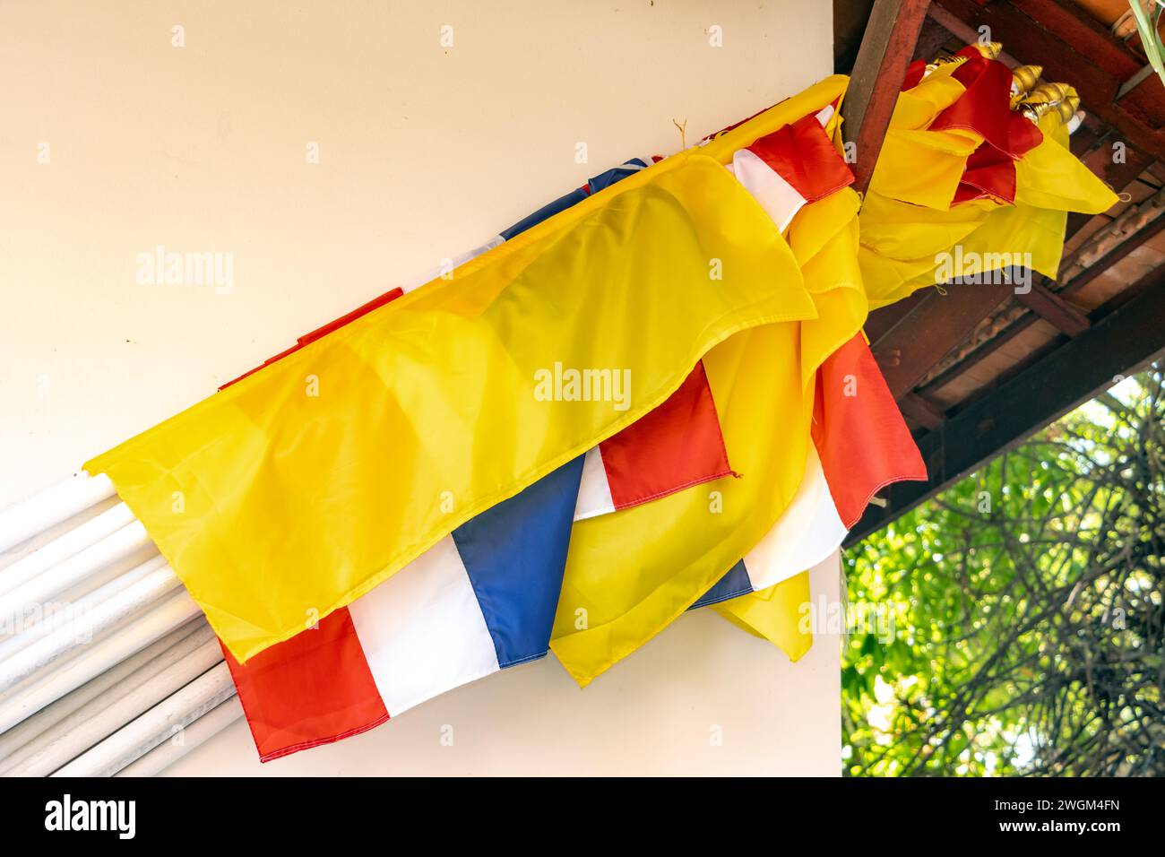 Una serie di bandiere nazionali thailandesi con bandiera buddista appoggiata al muro di un edificio in un tempio buddista Foto Stock