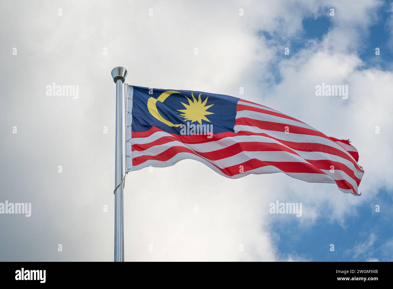 Bandiera della Malesia legata a un palo che sventola contro il cielo blu e le nuvole. Foto Stock