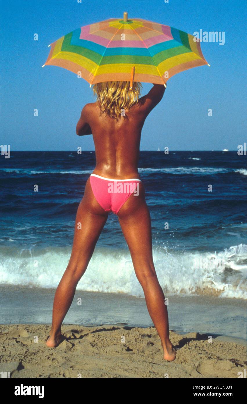 bella capelli biondi silhouette giovane donna abbronzante corpo sano naturale acqua di mare blu sfondo fitness con ombrello Foto Stock