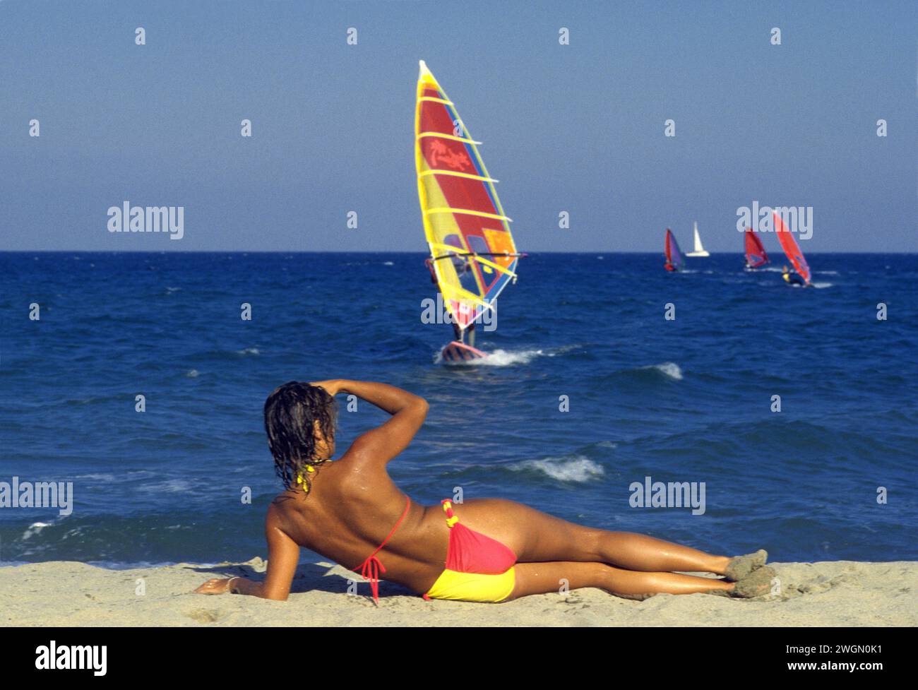sport windsurfer capelli scuri bella donna può giù sulla sabbia per tornare a fotocamera cielo blu e sfondo di acqua di mare Foto Stock