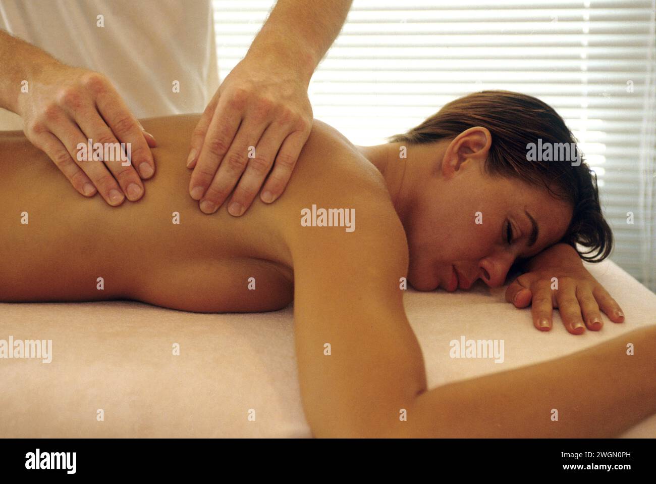 grazioso tavolo da massaggio spa naturale per la schiena con i capelli di auburn e le mani di una massaggiatrice con luce rilassante Foto Stock