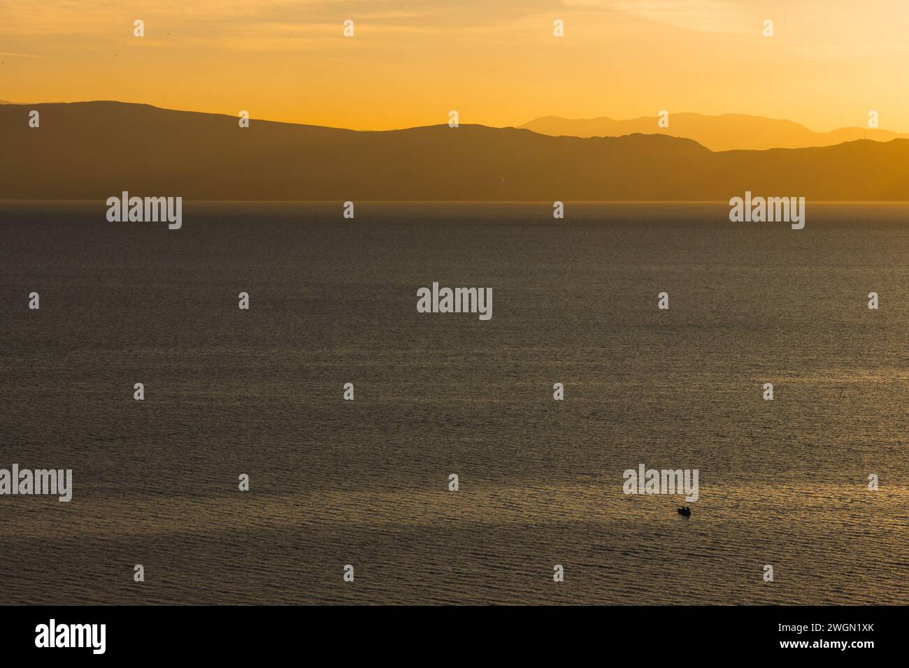 Ora d'oro al tramonto sul lago di Ocrida nella Macedonia del Nord, con uno splendido sfondo di montagna e una barca lontana da sola sulle acque calme del lago. Foto Stock