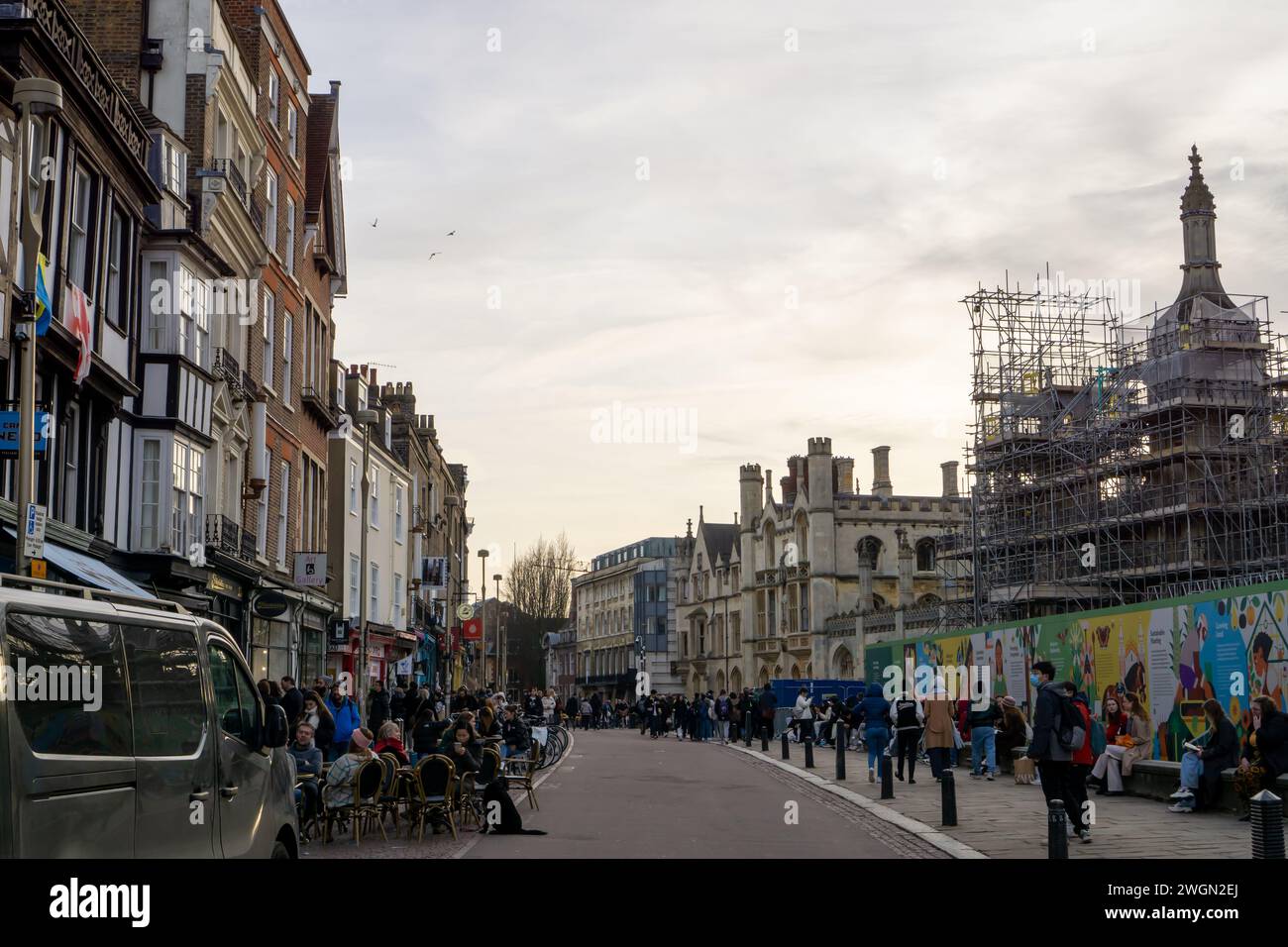 I turisti sono in un pomeriggio nuvoloso a piedi e seduti fuori dai caffè della Kings Parade a Cambridge nel Regno Unito Foto Stock