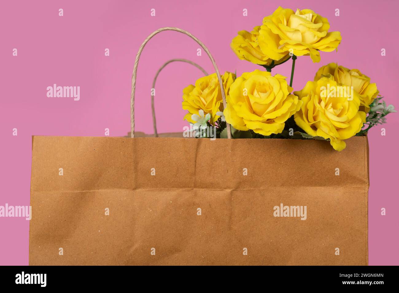 Bouquet di rose gialle in un sacchetto di carta su sfondo rosa Foto Stock