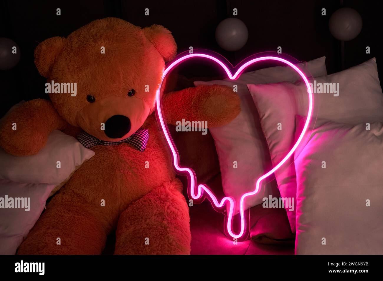 Orsacchiotto marrone giace nei cuscini e contiene un cuore rosa al neon. San Valentino 14 febbraio, Gift Romantic background. Dichiarazione d'amore, congratulazioni Foto Stock