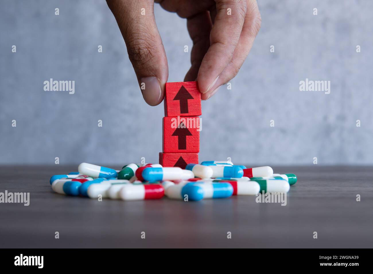 Un blocco di legno rosso con freccia rivolta verso l'alto su una pila di pillole colorate. Aumento dei costi del concetto di farmaci soggetti a prescrizione medica. Foto Stock