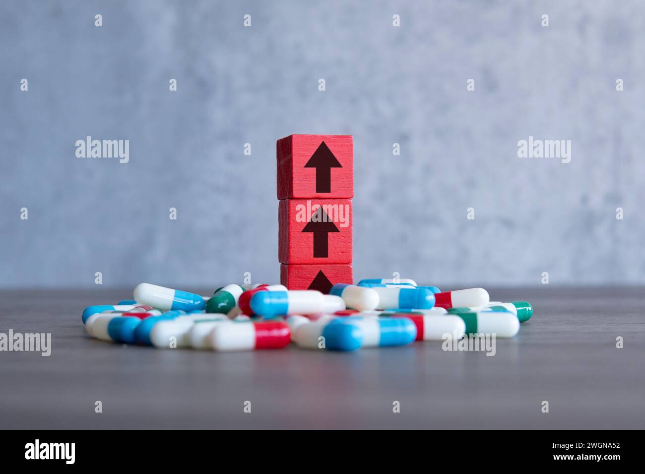 Un blocco di legno rosso con freccia rivolta verso l'alto su una pila di pillole colorate. Aumento dei costi del concetto di farmaci soggetti a prescrizione medica. Foto Stock