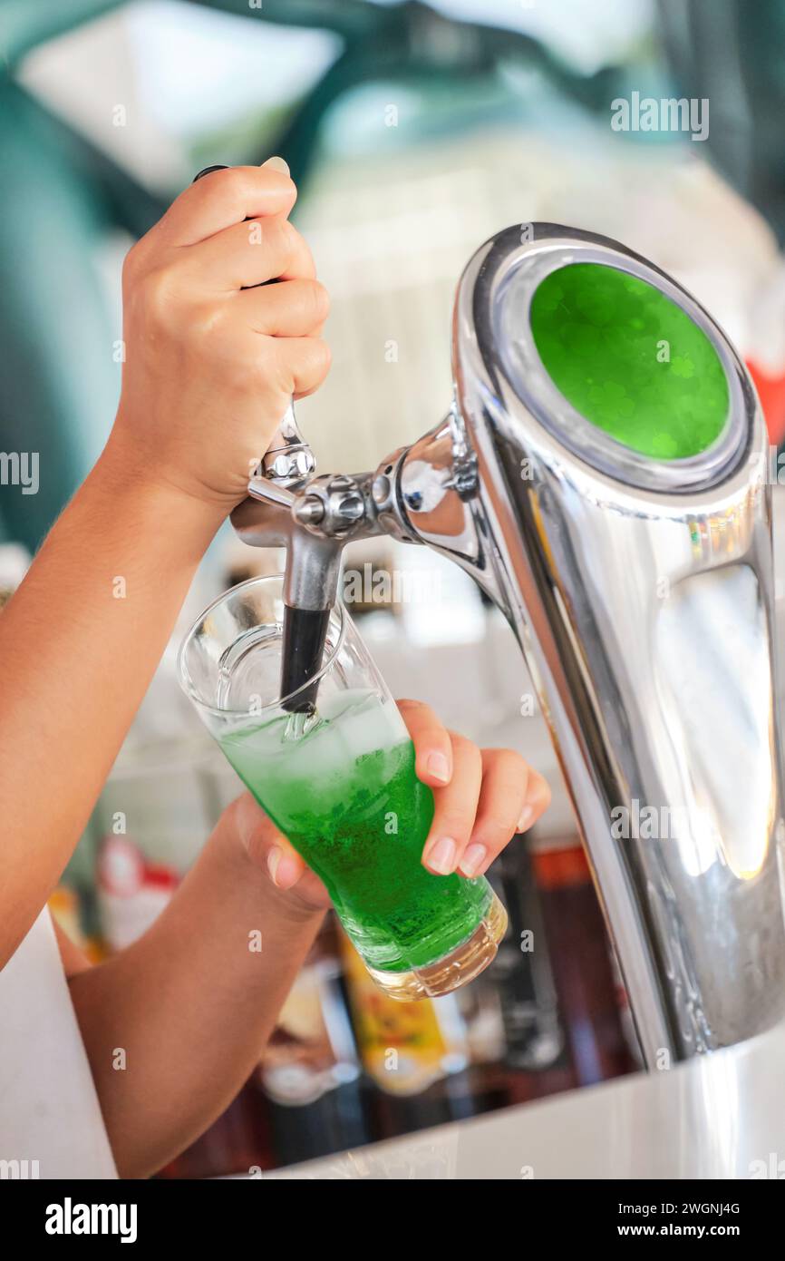 Un barista versa birra verde in una tazza di vetro in un bar durante un St. Festa di Patrick Foto Stock