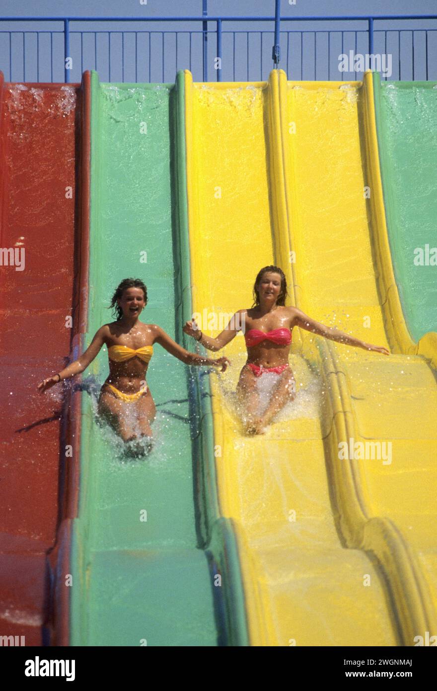 2 graziose giovani donne di capelli biondi scivolano verso il parco acquatico di plastica per toboga sorridendo Foto Stock