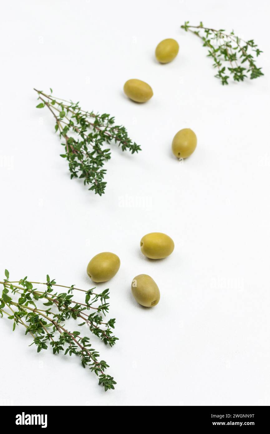 Ciuffi di timo e olive in tavola. Sfondo bianco. Posizione piatta. Foto Stock