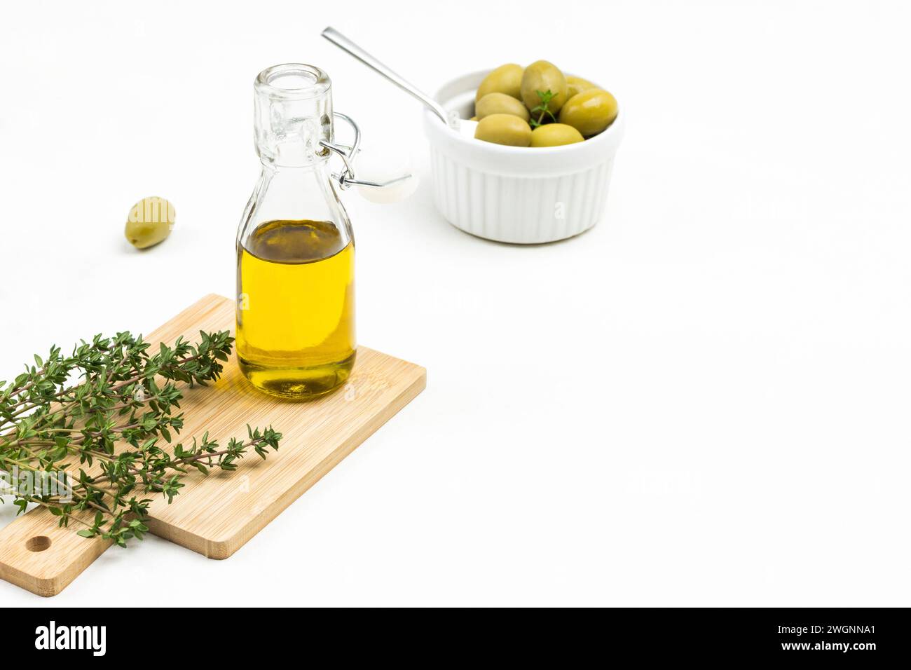 Bottiglia di olio d'oliva e ciuffi di timo a bordo. Olive in un recipiente di ceramica. Copia spazio. Sfondo bianco. Vista dall'alto. Foto Stock