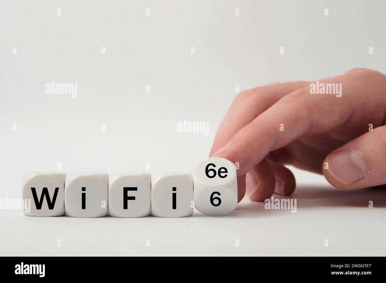 La mano gira i dadi e cambia l'espressione "WiFi 6" in "WiFi 6e" su sfondo bianco Foto Stock