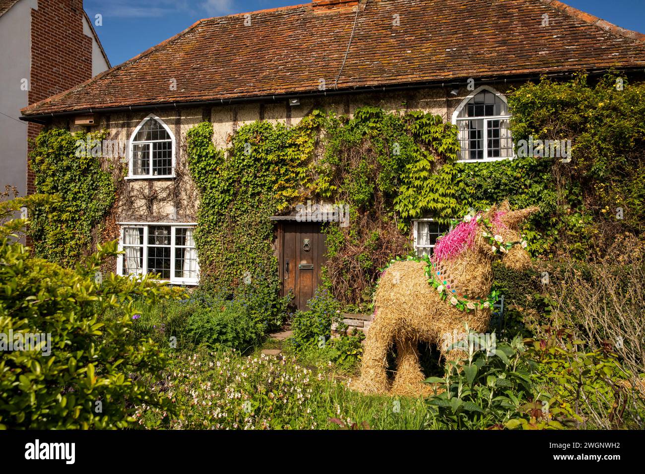 Regno Unito, Inghilterra, Suffolk, East Bergholt, The Street, unicorno di paglia nel giardino di cottage rivestiti di edera Foto Stock