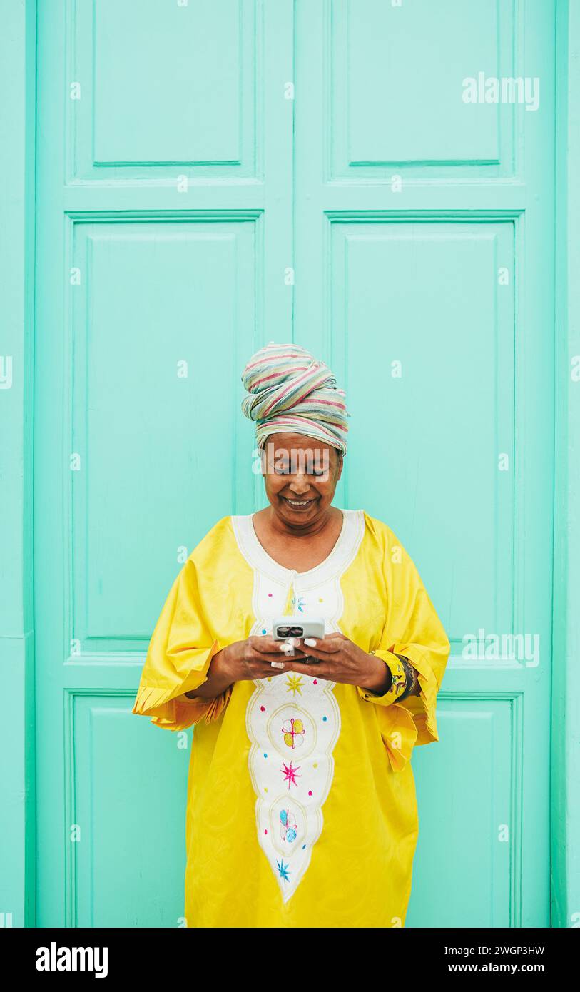 Donna anziana africana che usa il telefono cellulare mentre indossa abiti etnici tradizionali - tecnologia, etnia e concetto di persone mature - foto verticale Foto Stock