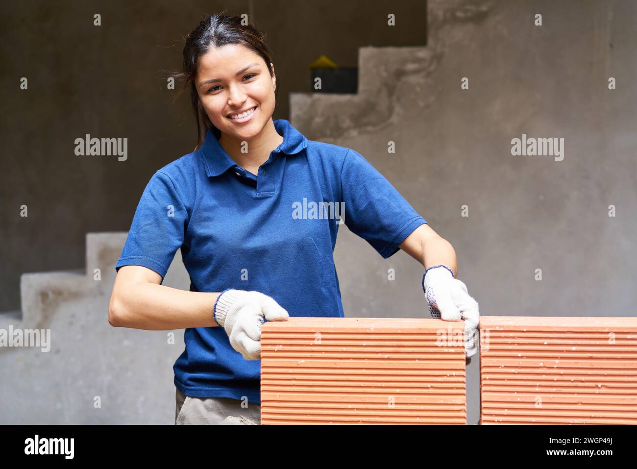 Donna sorridente che mette mattoni sulla parete Foto Stock