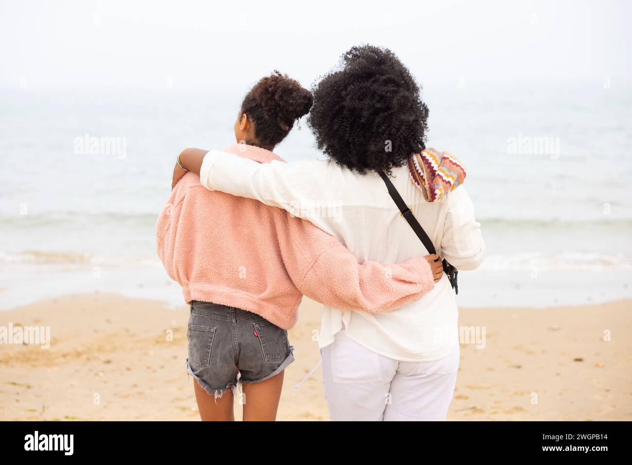 Due sorelle miste sulla spiaggia si abbracciano e si affacciano sul mare. Foto Stock