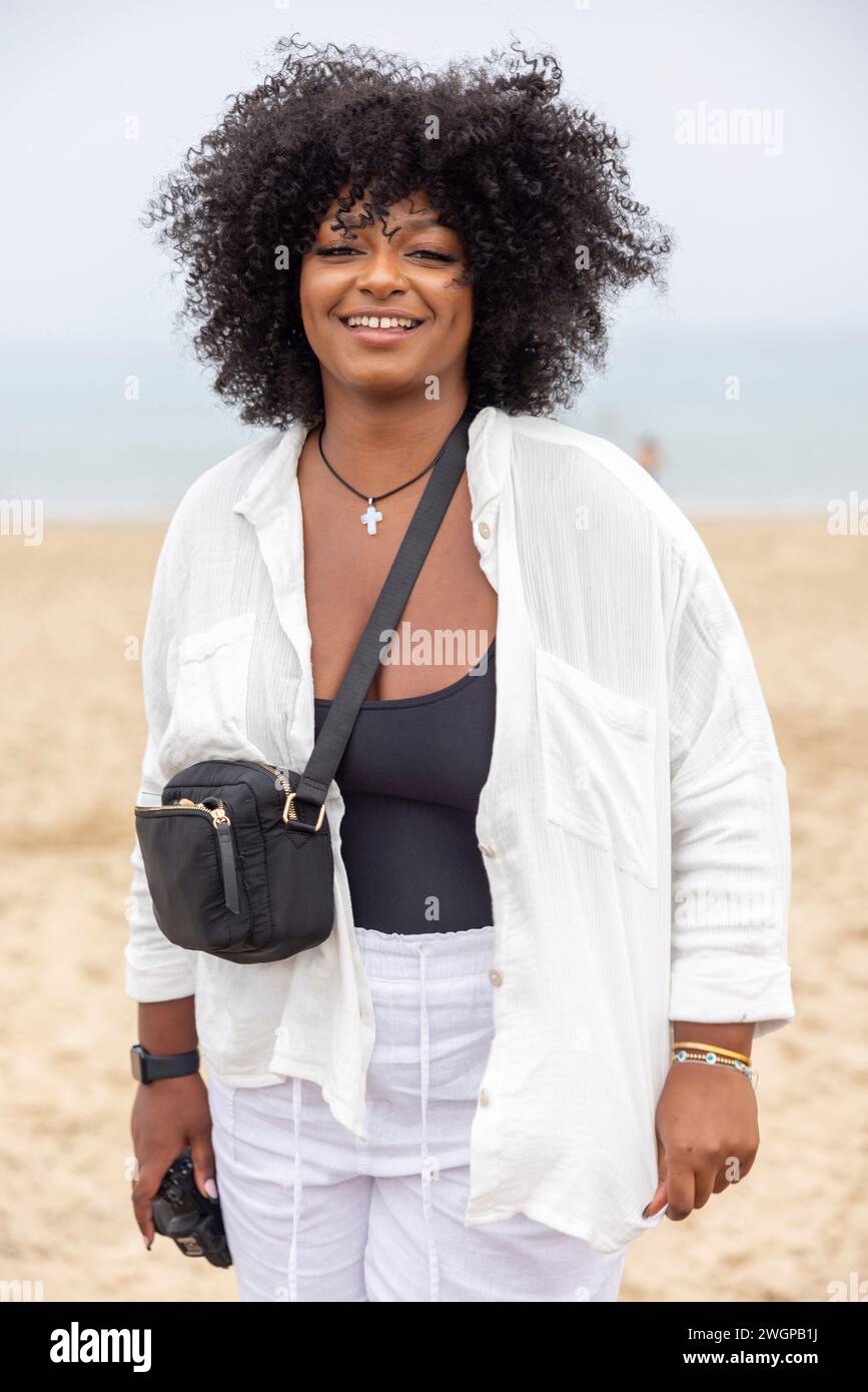 Un ritratto di una giovane donna nera sulla spiaggia, sta sorridendo nella macchina fotografica Foto Stock