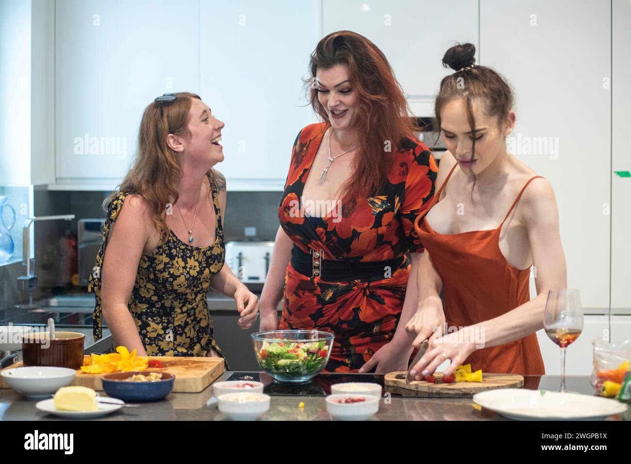 Un gruppo misto di amiche che si divertono e ridono mentre preparano cibo da festa in una cucina moderna Foto Stock