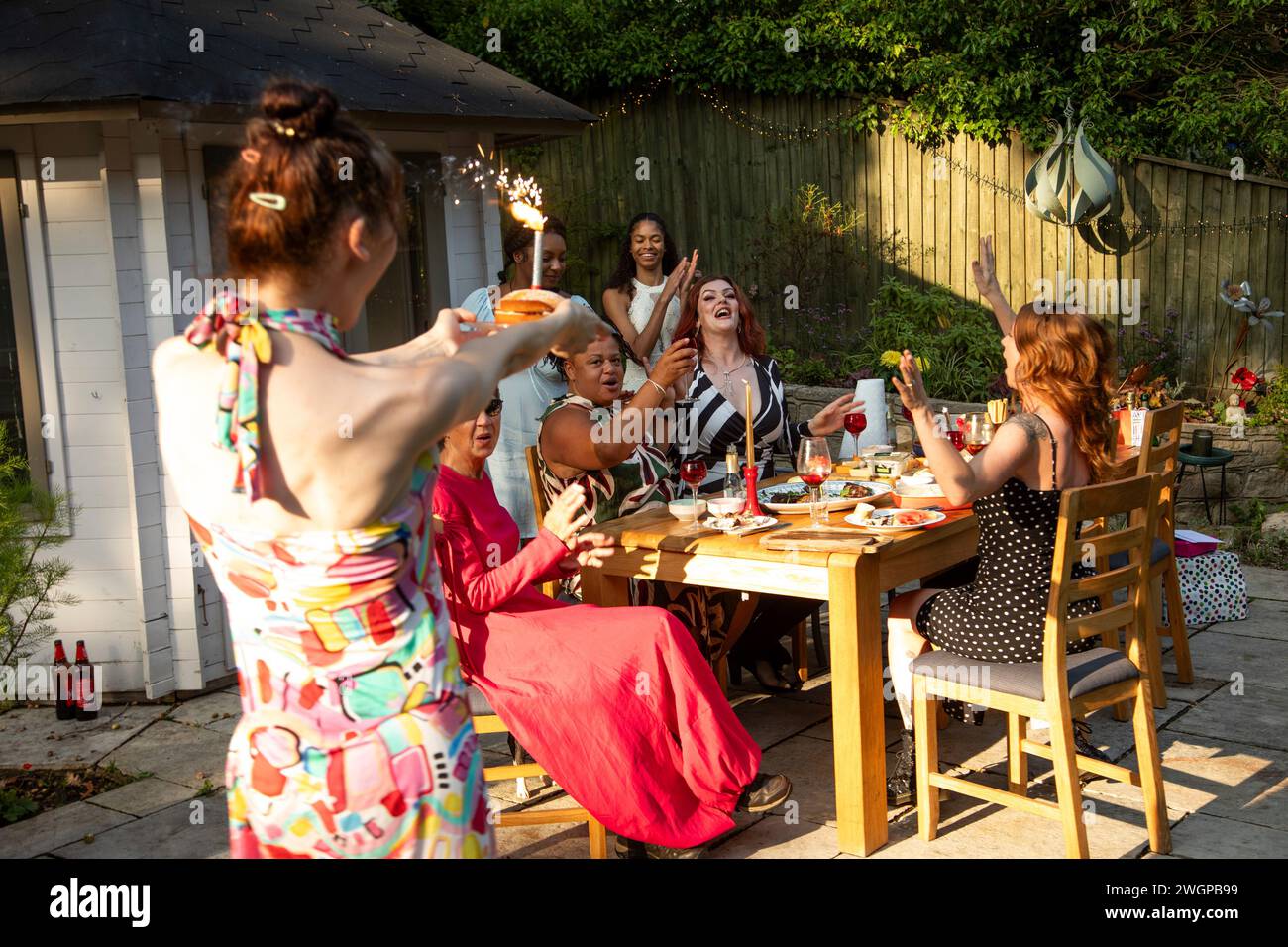 Un incontro misto di donne che ridono e si divertono durante una festa di compleanno estiva in giardino, pranzo Foto Stock