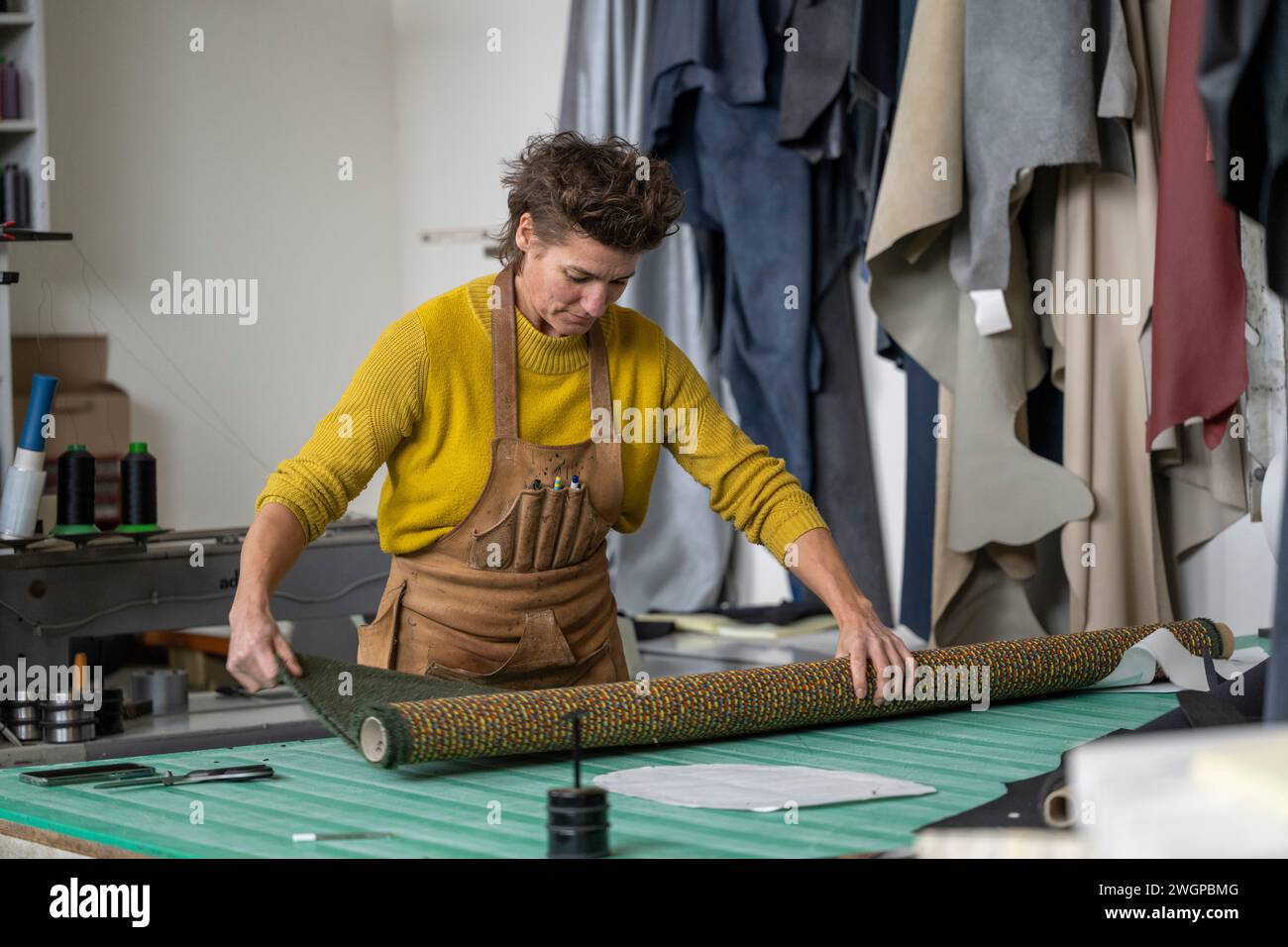 Nederland - Illustratief beeld. Meubelstoffeerder a haar werkplaats. Op de werkbank ligt stof op de rol en achter haar hangen stukken leer. foto: ANP / Hollandse Hoogte / Patricia Rehe Foto Stock