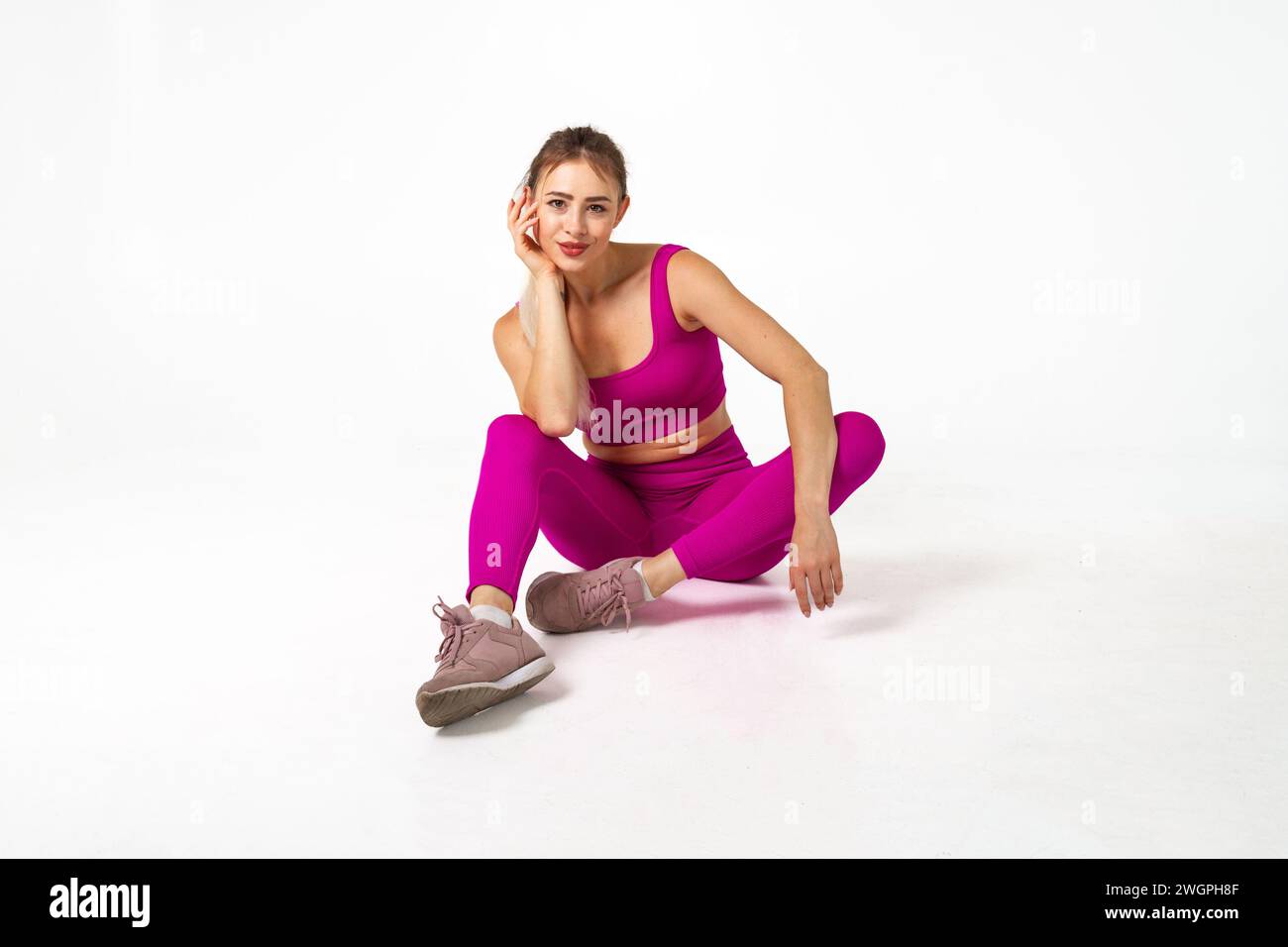 Donna in un vivace abito sportivo rosa seduta sul pavimento con gomito al ginocchio e mano contro il viso Foto Stock