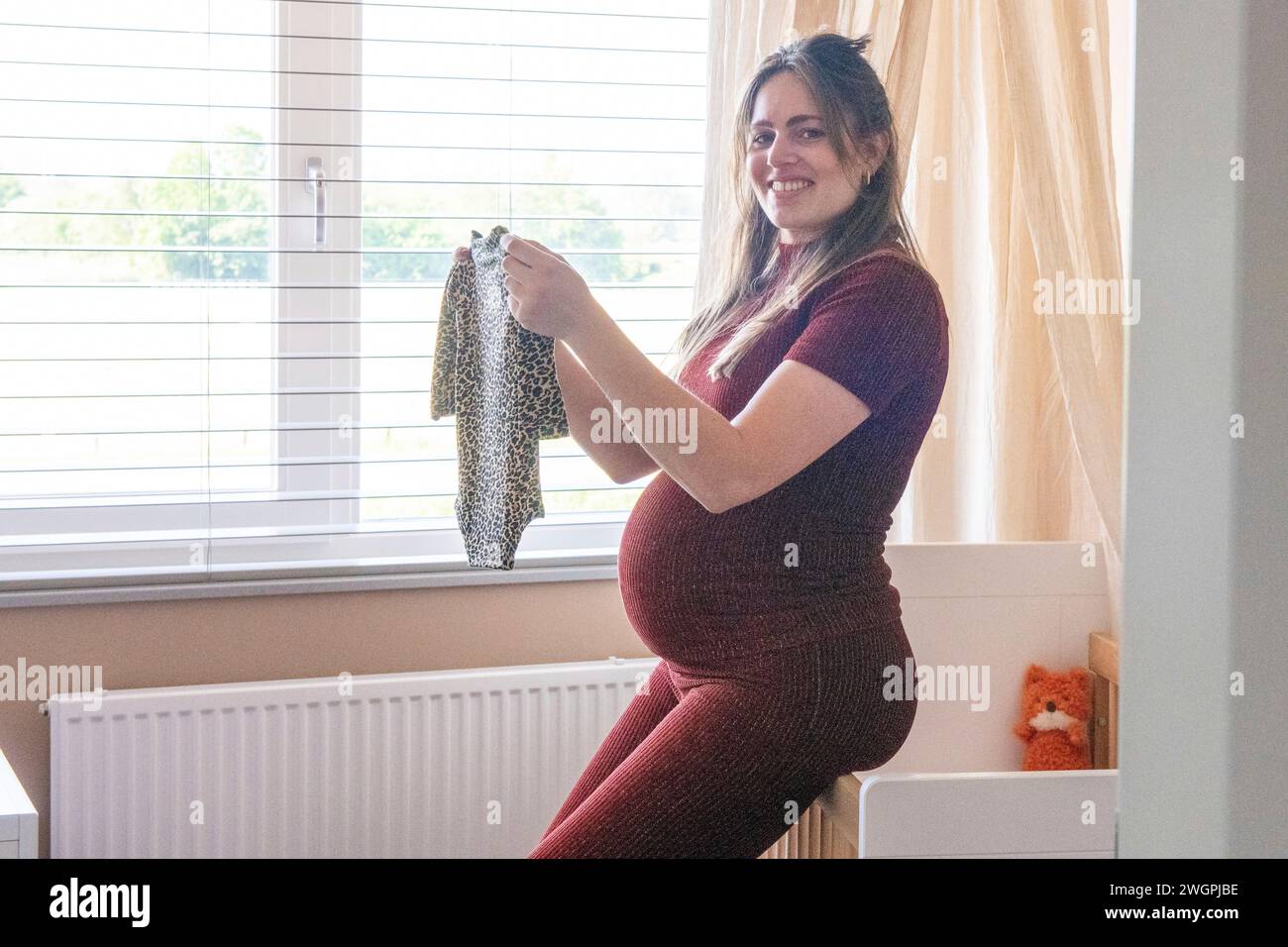 Madre felice incinta che si prende una pausa mentre pulisce i vestiti Foto Stock