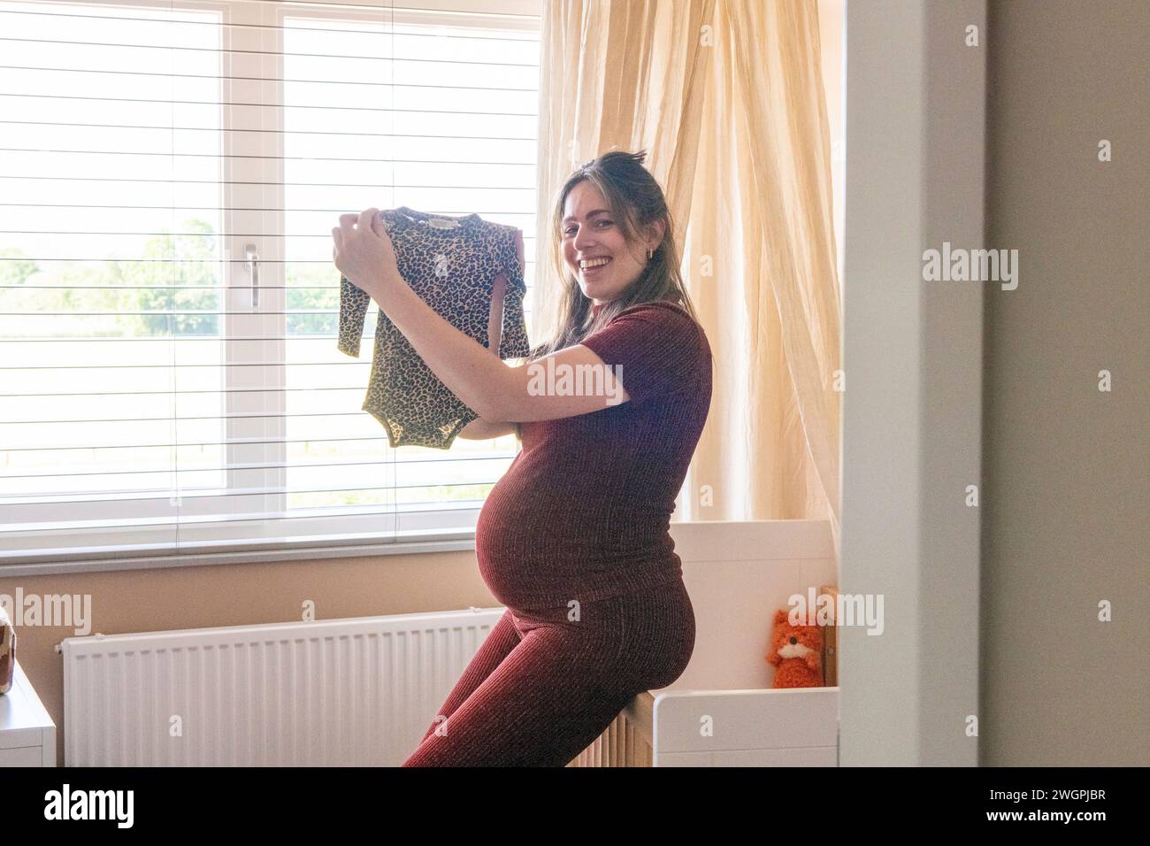 Madre felice incinta che si prende una pausa mentre pulisce i vestiti Foto Stock