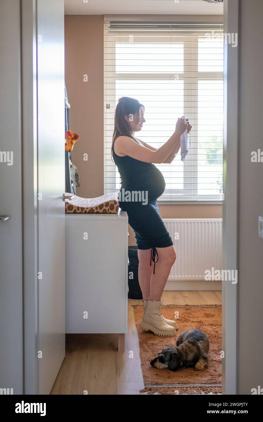 Madre incinta felice di aprire nuovi vestiti per il bambino Foto Stock