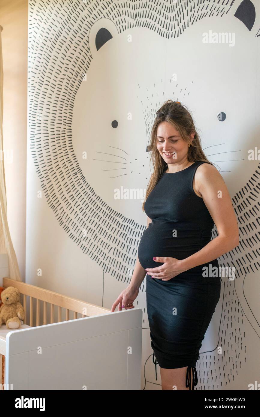 Felice ritratto di una madre incinta in piedi accanto alla sua culla Foto Stock