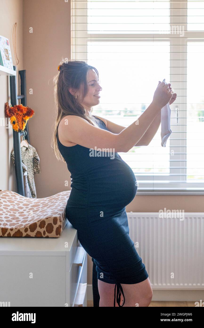 Madre incinta felice di aprire nuovi vestiti per il bambino Foto Stock