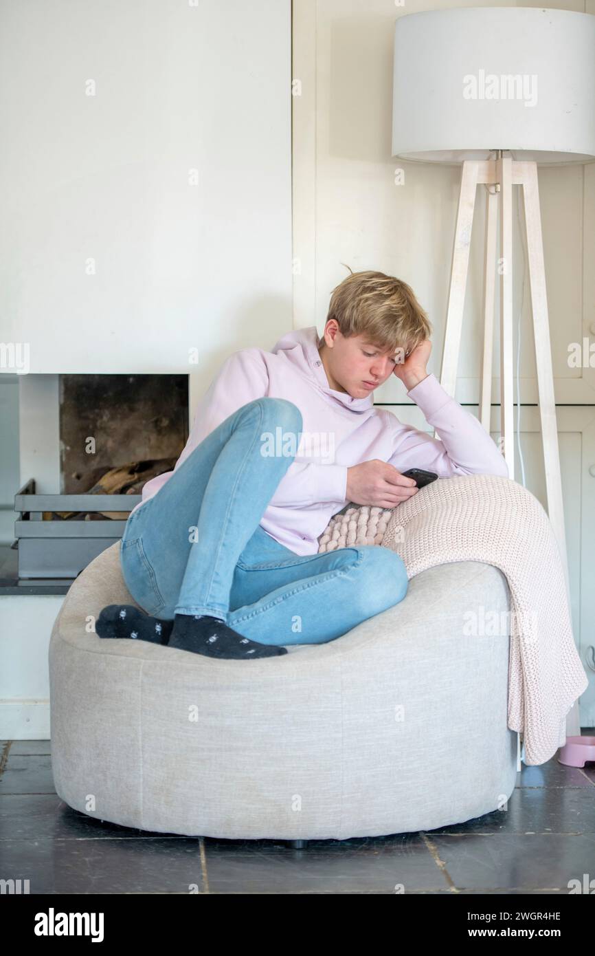 Un giovane uomo seduto sul divano in una casa moderna e pulita con il telefono che naviga Foto Stock