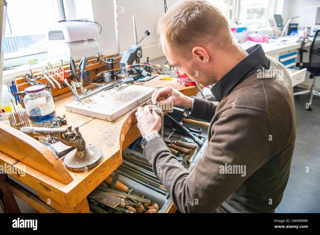 Orologiaio che ripara un orologio classico, luogo di lavoro autentico. Utilizzo di un monocle e piccoli utensili per le riparazioni Foto Stock