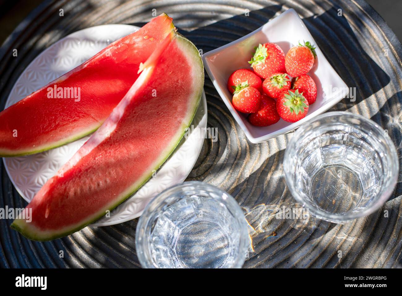 Primo piano di fragole di melone al sole estivo, tavola e bicchieri d'acqua a lato Foto Stock