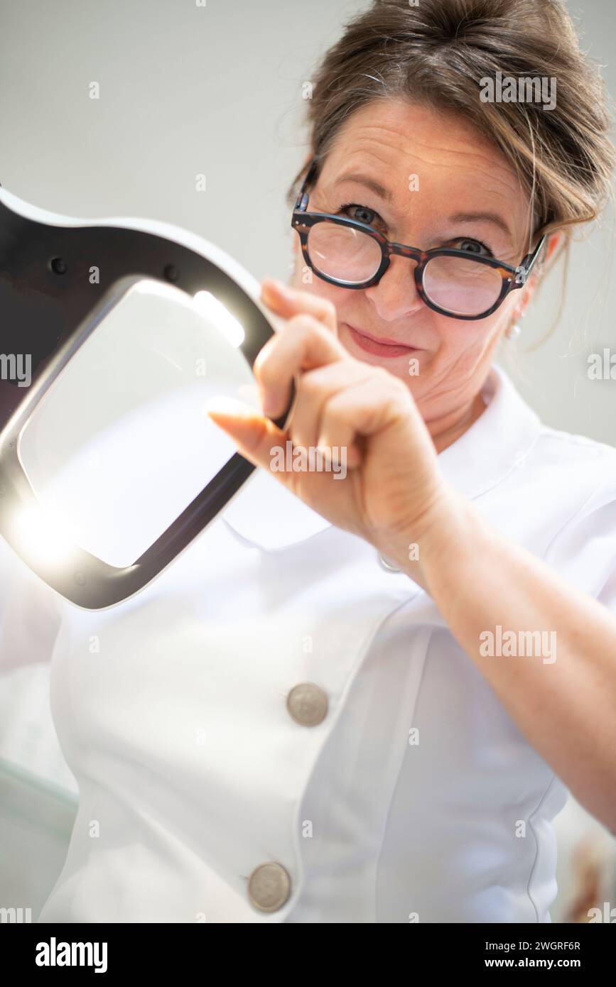 ritratto della bruna estetista che guarda attraverso una lente d'ingrandimento la sua paziente Foto Stock