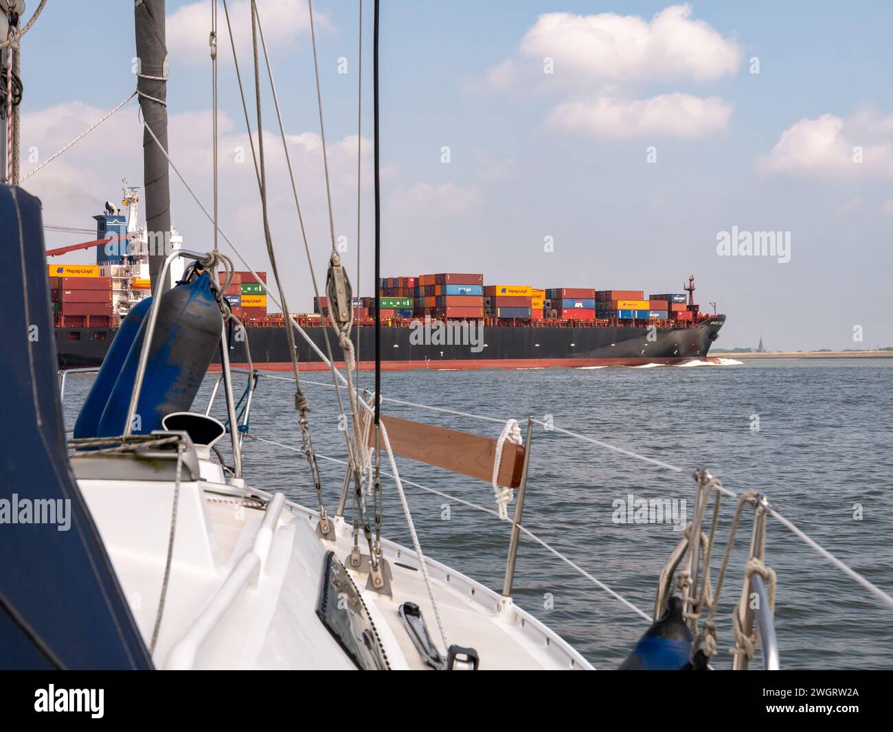 Barca a vela che attraversa Westerschelde nei Paesi Bassi, in attesa della nave portacontainer Spartel Trader diretta ad Anversa, Belgio Foto Stock