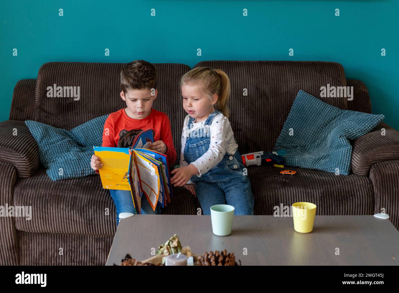 Fratello e sorella che si uniscono seduti insieme sul divano a leggere un libro di storie Foto Stock