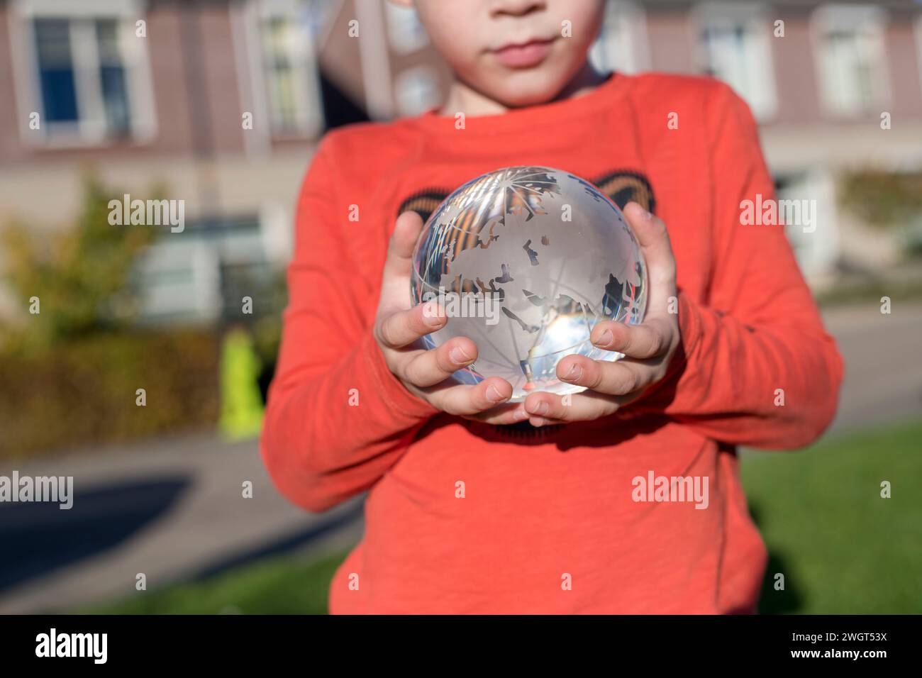 Bambino che tiene un globo di vetro in un parco pubblico, luce riflettente e vetro trasparente Foto Stock