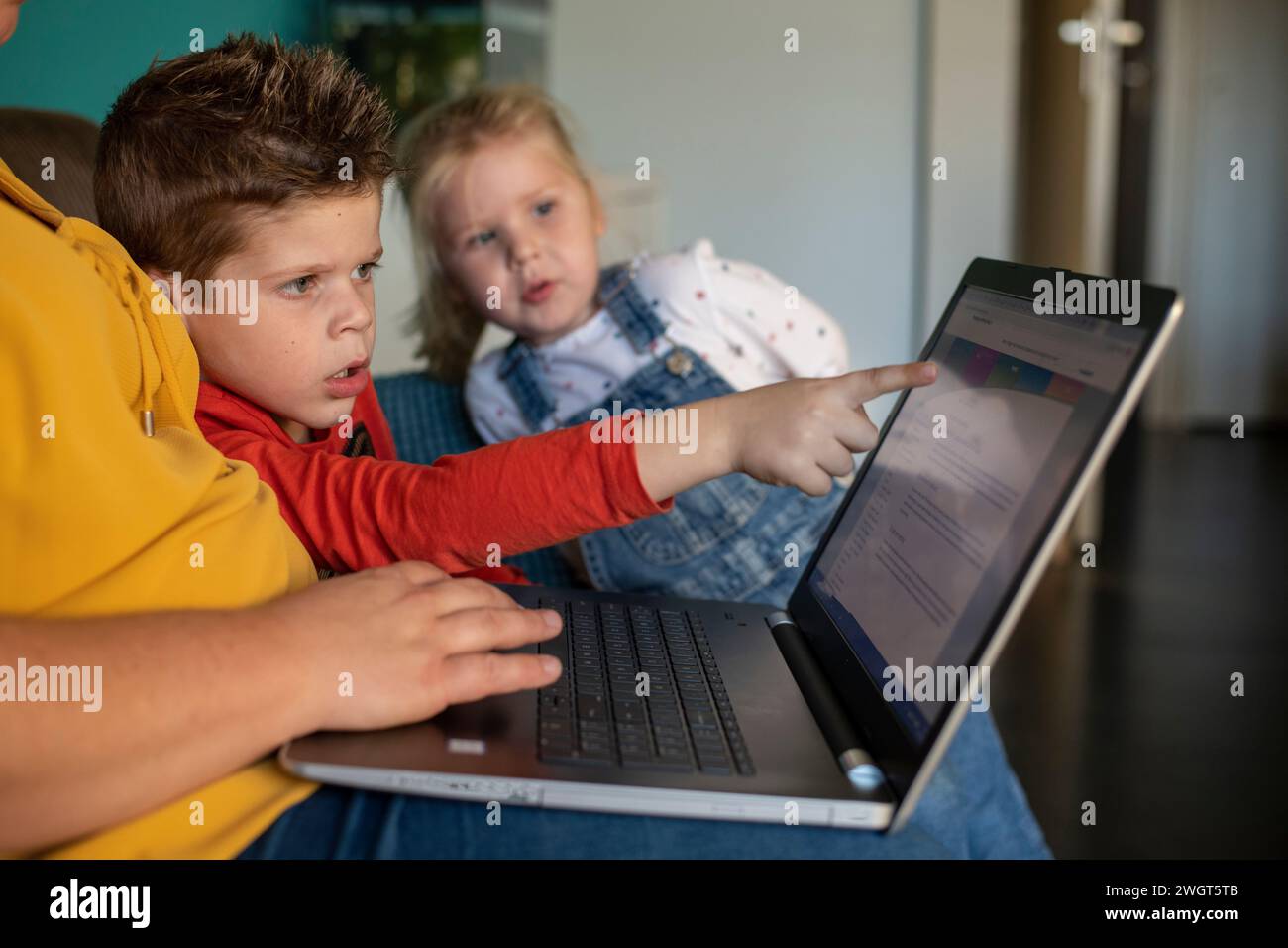 Madre seduta con suo figlio e sua figlia che lo educano e gli insegnano usando un portatile Foto Stock