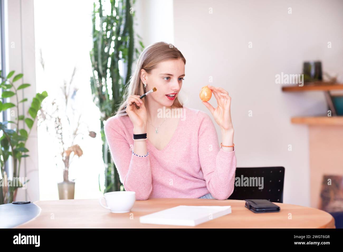 la giovane donna con i capelli biondi pratica il trucco con un uovo Foto Stock