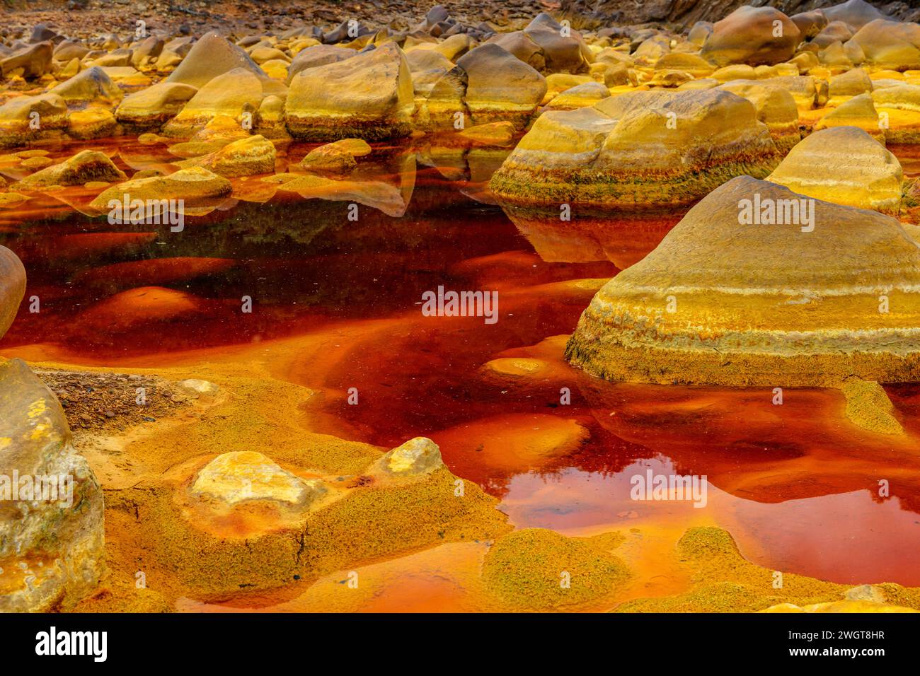 Pietre rivestite di ferro a strati emergono dalle acque acide e rossastre nell'esclusivo paesaggio del Rio Tinto Foto Stock